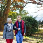 Senior woman and caregiver outdoors on a walk in park, talking.